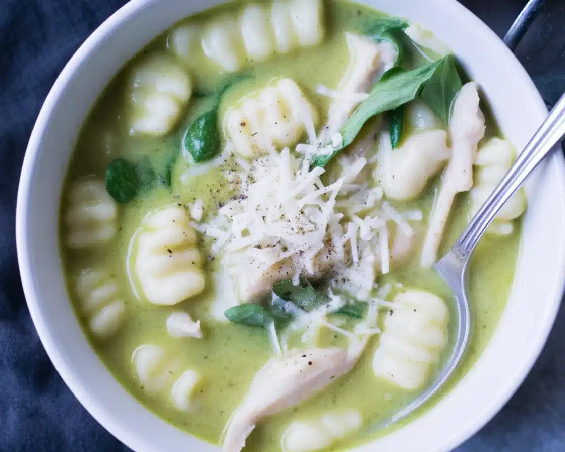 Deliciously Creamy Pesto Chicken Gnocchi Soup to Savor 1 Creamy Pesto Chicken Gnocchi Soup served in a bowl with fresh spinach and herbs.